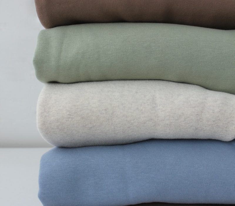 Neatly Folded Pastel Hoodies, Closet Order. A Stack Of Knitted Jumpers In Delicate Beige, Blue And L Neatly folded pastel hoodies, closet order. A stack of knitted jumpers in delicate beige, blue and light green tones. cozy fabric texture.